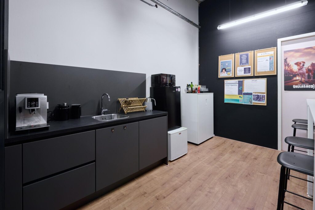 Keukenruimte in een kantoor aan de Johan Huizingalaan met een koffiezetapparaat, spoelbak, koelkast en prikborden aan de muur.